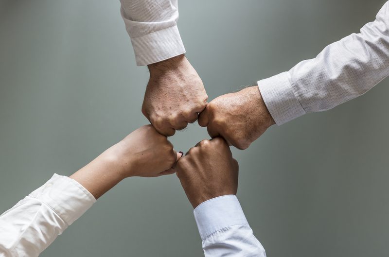 Four colleagues joining hands in the centre of a circle